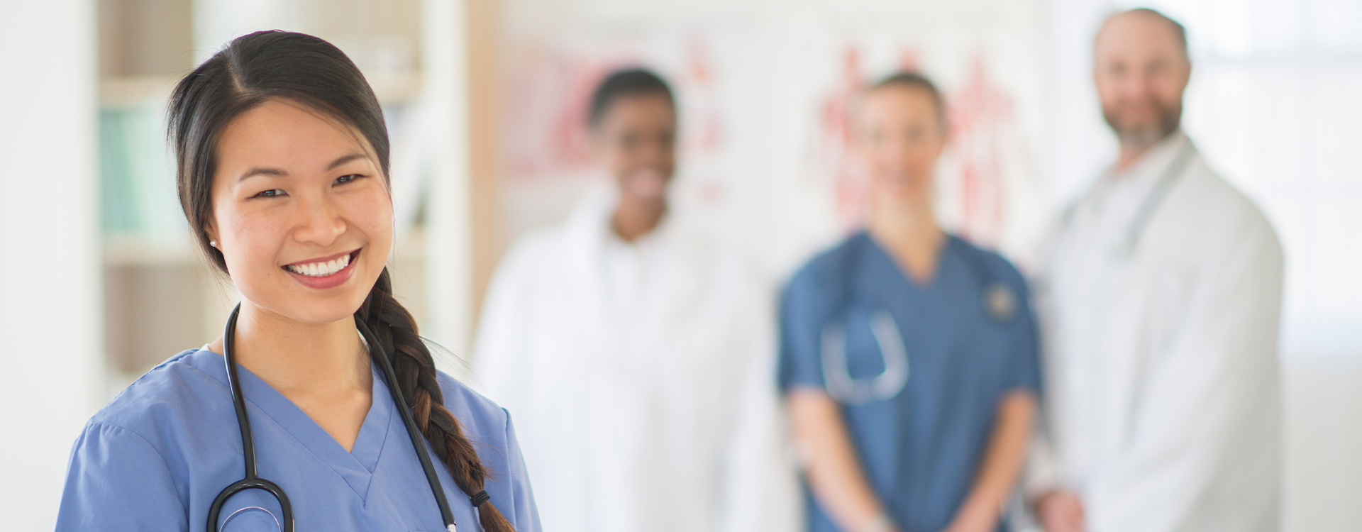 young doctor in blue scrubs smiling, group of medical professionals behind her smiling