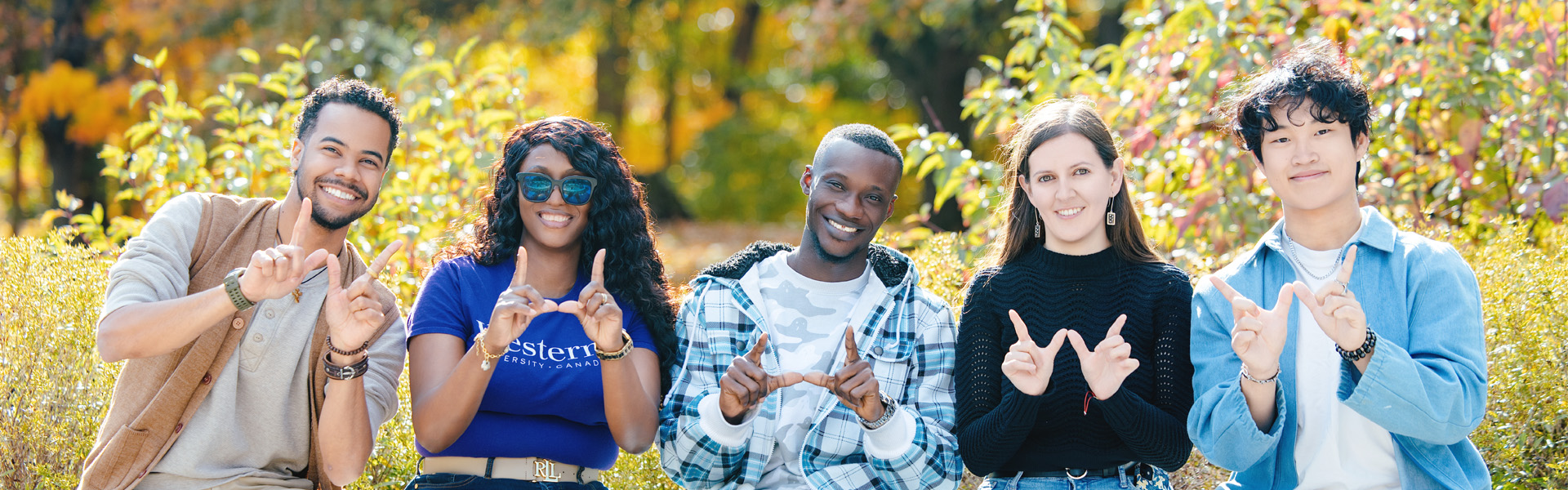 5 students smiling and holding up the Western "W" in the fall