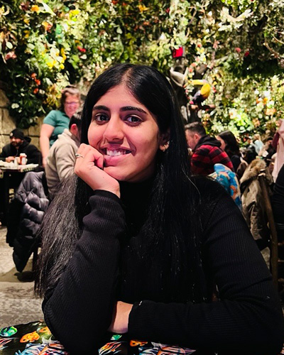 A student with black hair smiling with foliage in the background
