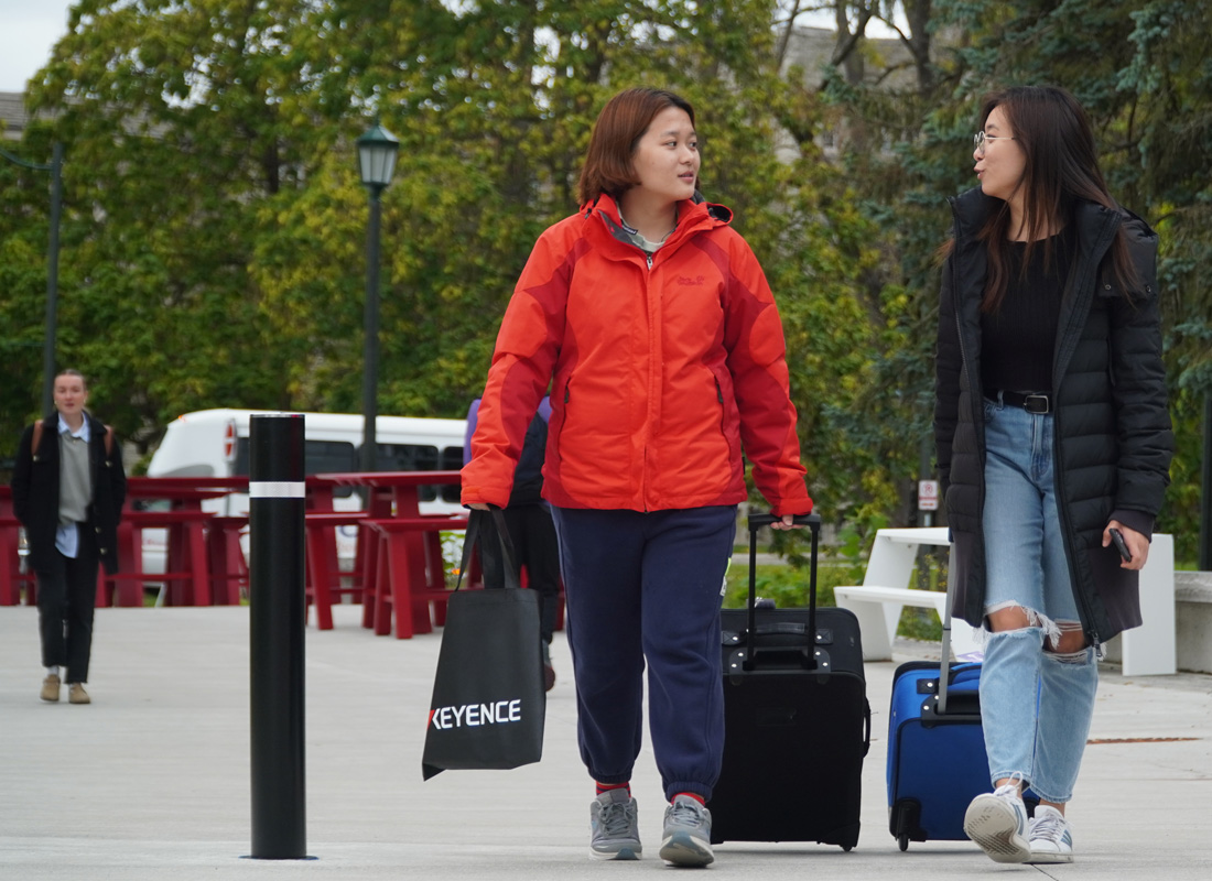 Two students with suitcases walking towards the camera