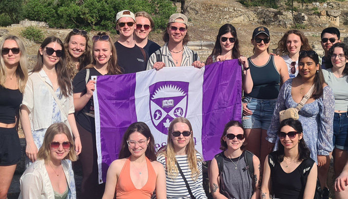 Dozens of students hold a Western Flag on a faculty led trip