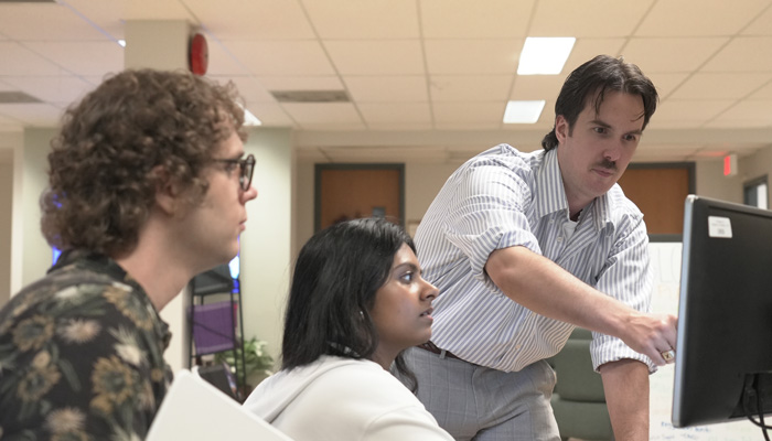 An intern and their supervisor discuss work on the computer