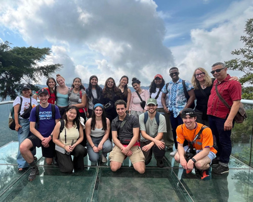 Students standing or crouched on a dock at a lake