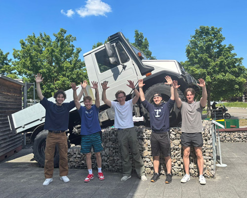 students standing in front of a truck with their hands in the air