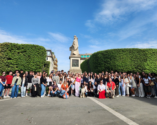 A bunch of students in front of a statue in Tuscany.