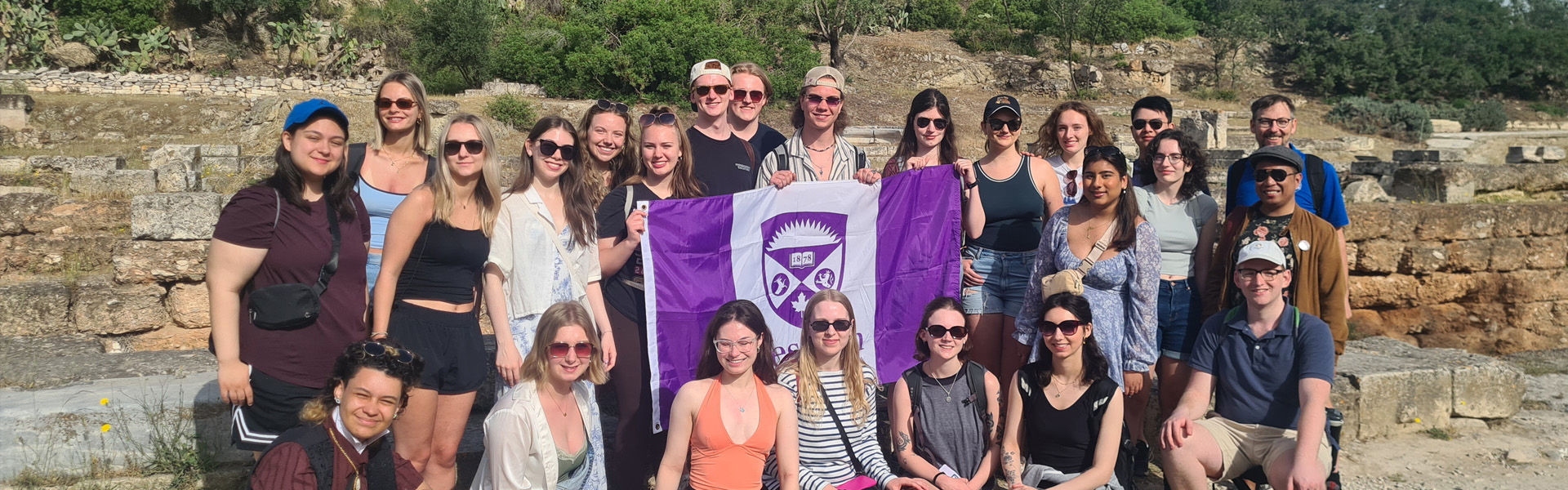 Students standing and smiling with a Western Flag on a Faculty-Led trip