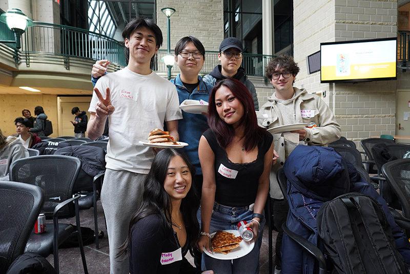 Students standing together in the IGAB atrium holding pizza