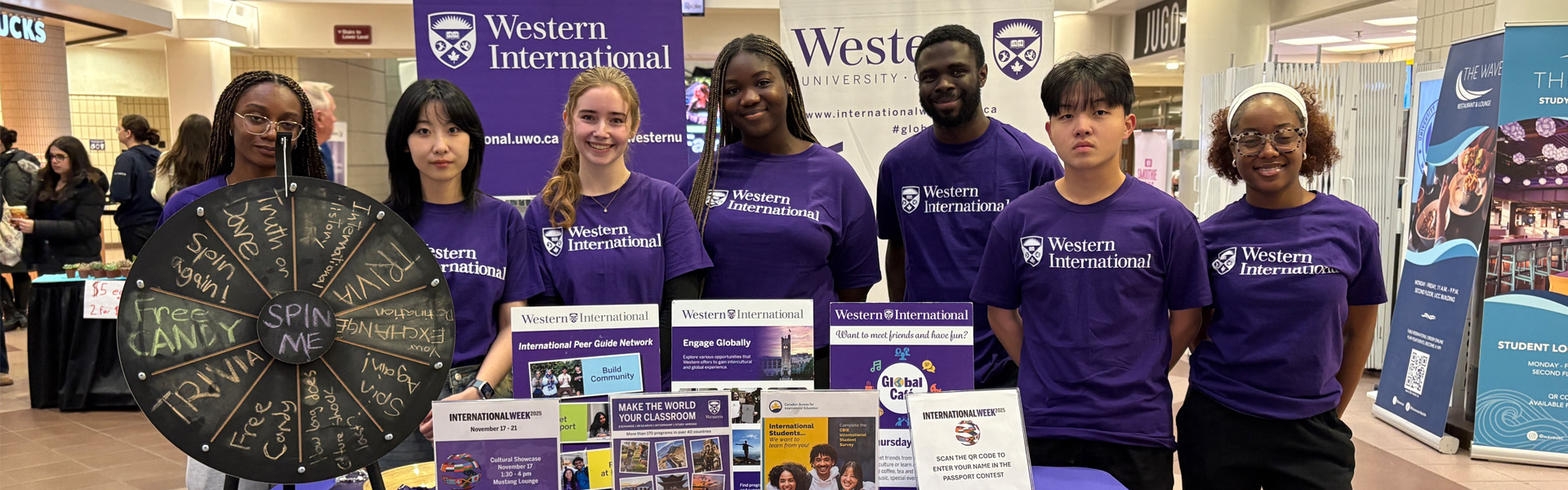 students standing in Western International t-shirts in front of the promotional booth where students can come and ask for information about Western International